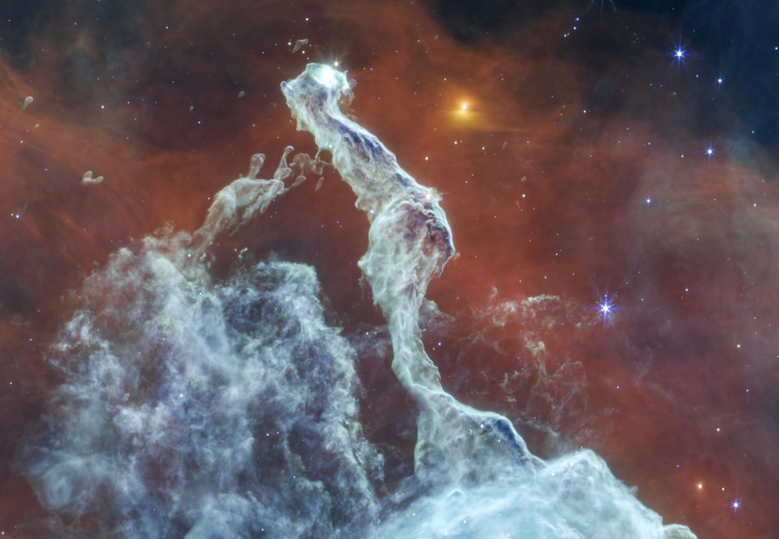 Webb MIRI mid-infrared image of the Cat's Head Nebula: a pale grey-blue pillar rising from a large billowing cloud at lower left, set against rusty red emission, with a bright orange-yellow point of light to the right of the pillar's head and scattered blue stars