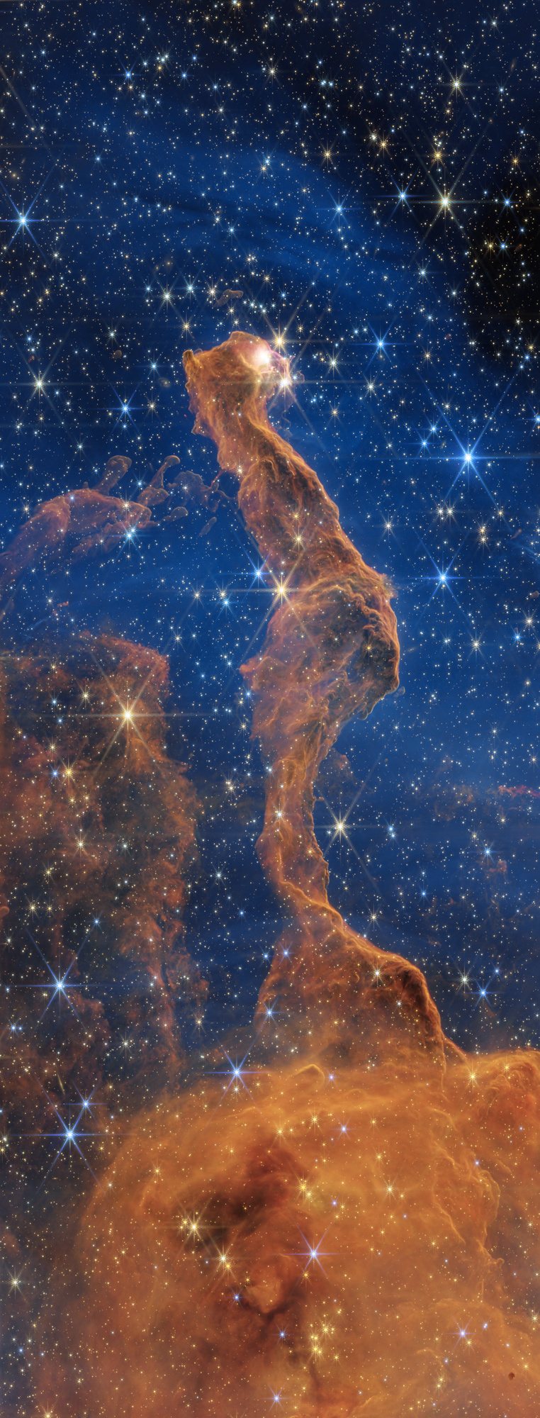 Webb NIRCam near-infrared image of the Cat's Head Nebula: a tall orange pillar with a yellow glowing point at its head, set against a deep blue background crowded with stars, with an orange cloud at the bottom of the frame