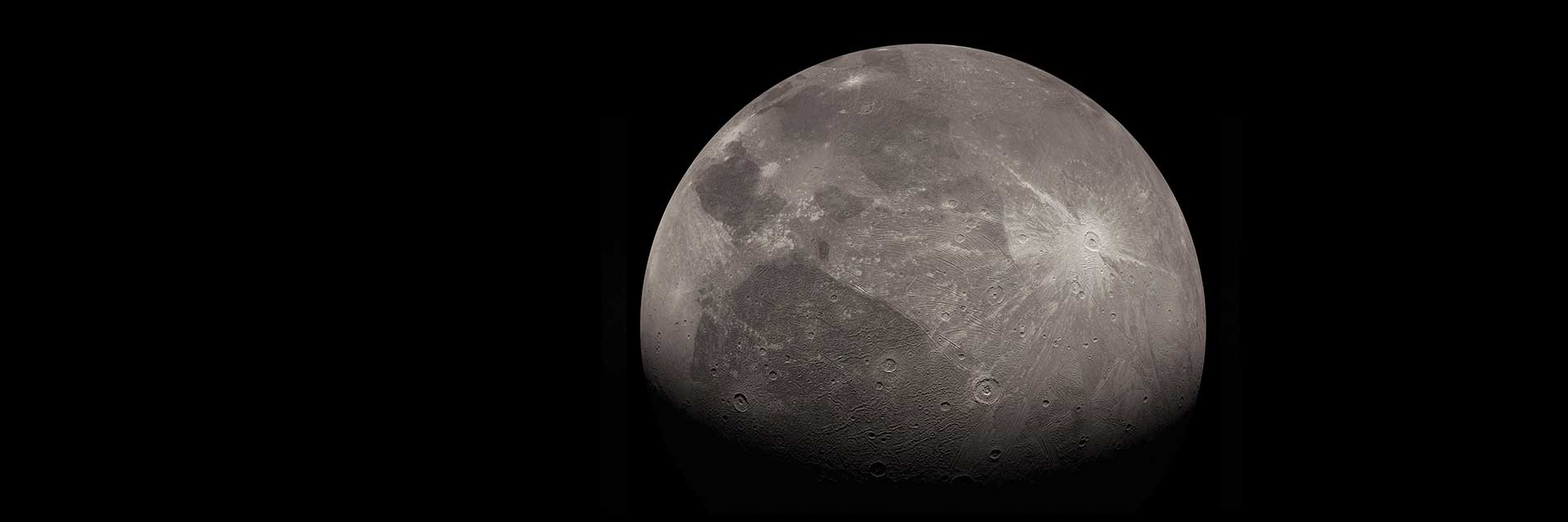 Jupiter's moon Ganymede — the largest moon in the solar system, larger than Mercury, showing dark cratered regions and lighter grooved terrain