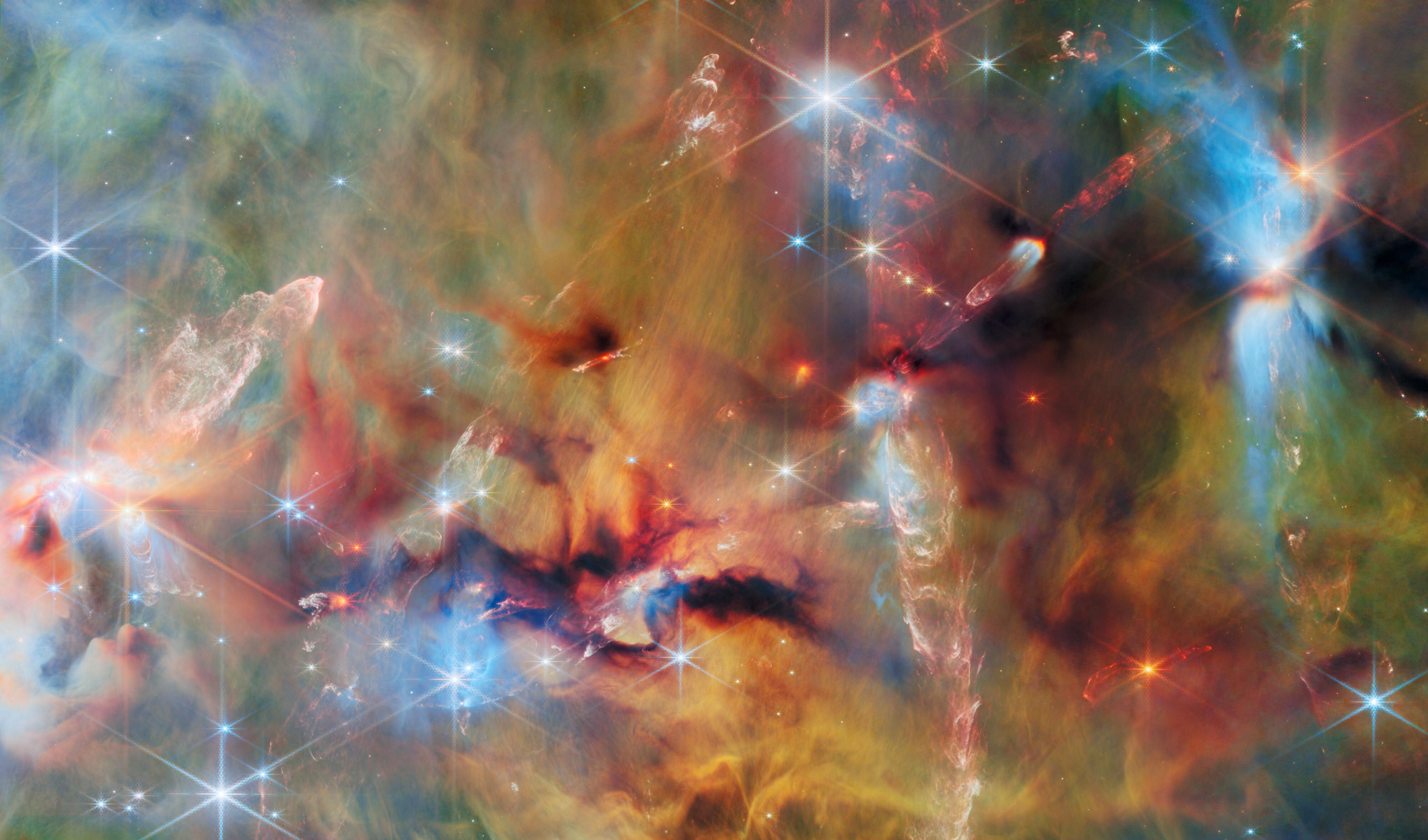 James Webb Space Telescope NIRCam image of Orion Molecular Cloud 2 (OMC-2) showing billowing orange and blue gas clouds, dark dusty globules, and brilliant young stars at every stage of formation