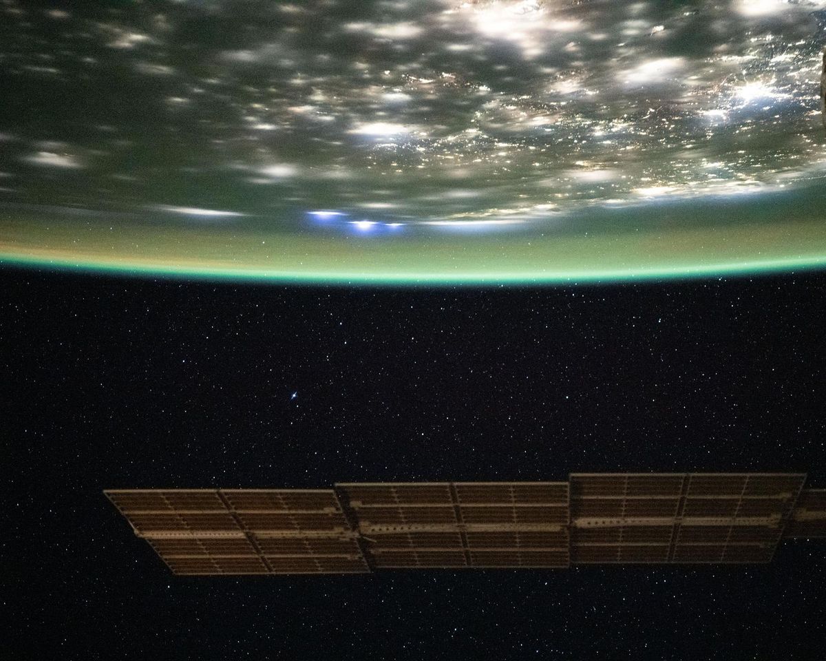 The city lights of the eastern United States under a layer of green airglow, with stars above, photographed from the International Space Station