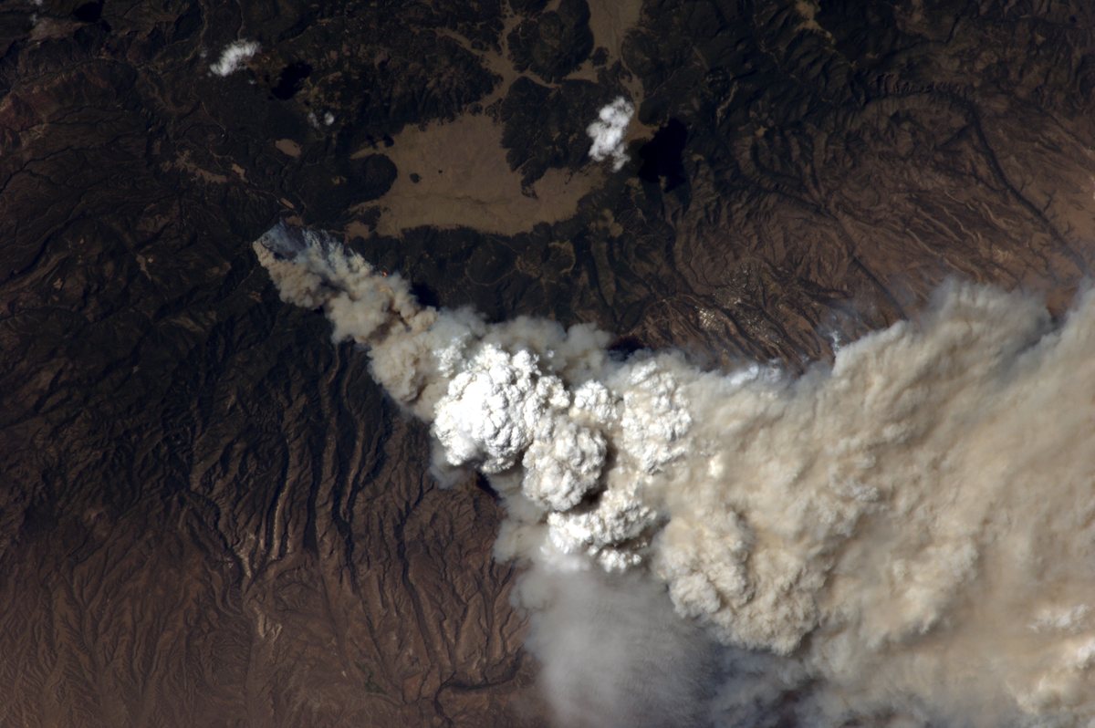 The forested Jemez Mountains of north-central New Mexico seen from the International Space Station, with a large smoke plume rising from the Las Conchas fire and pale grassland openings beyond it