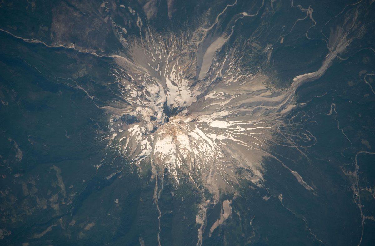 Snow-capped Mount Hood and its glaciers surrounded by dark forest, photographed from the International Space Station