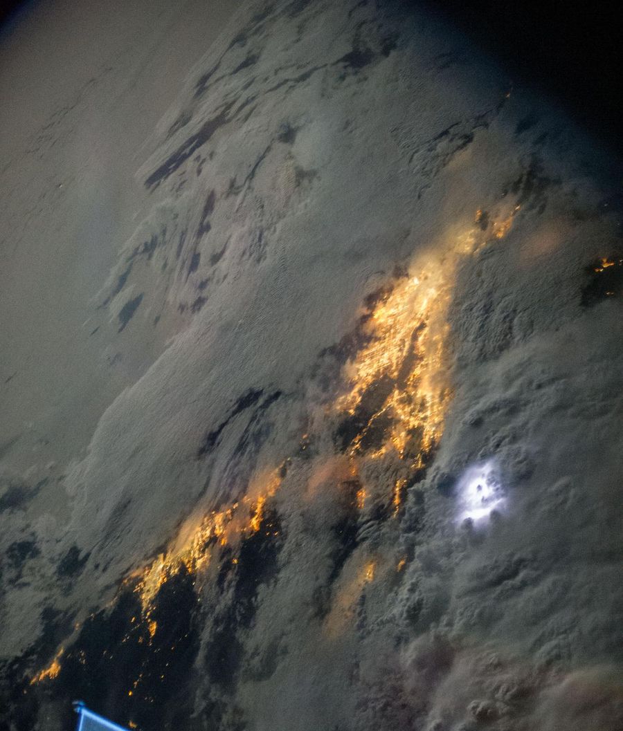 Southern California at night from the International Space Station with city lights glowing through a low cloud deck and a lightning flash