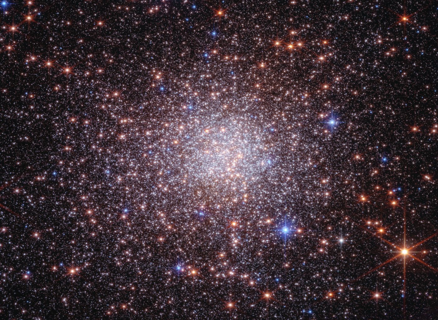 Thousands of stars in Terzan 5 captured by NASA's Webb and Hubble space telescopes — a dense, circular orb of white, orange, and blue stars against the black backdrop of space, with prominent diffraction spikes on the brightest stars