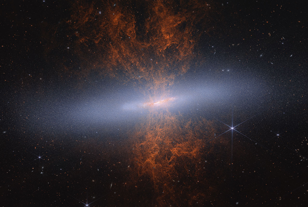 NASA Webb NIRCam composite image of the Cigar Galaxy M82 — a chaotic starburst galaxy with glowing filaments and outflow plumes of orange and red extending above and below a bright central core, set against a field of surrounding stars