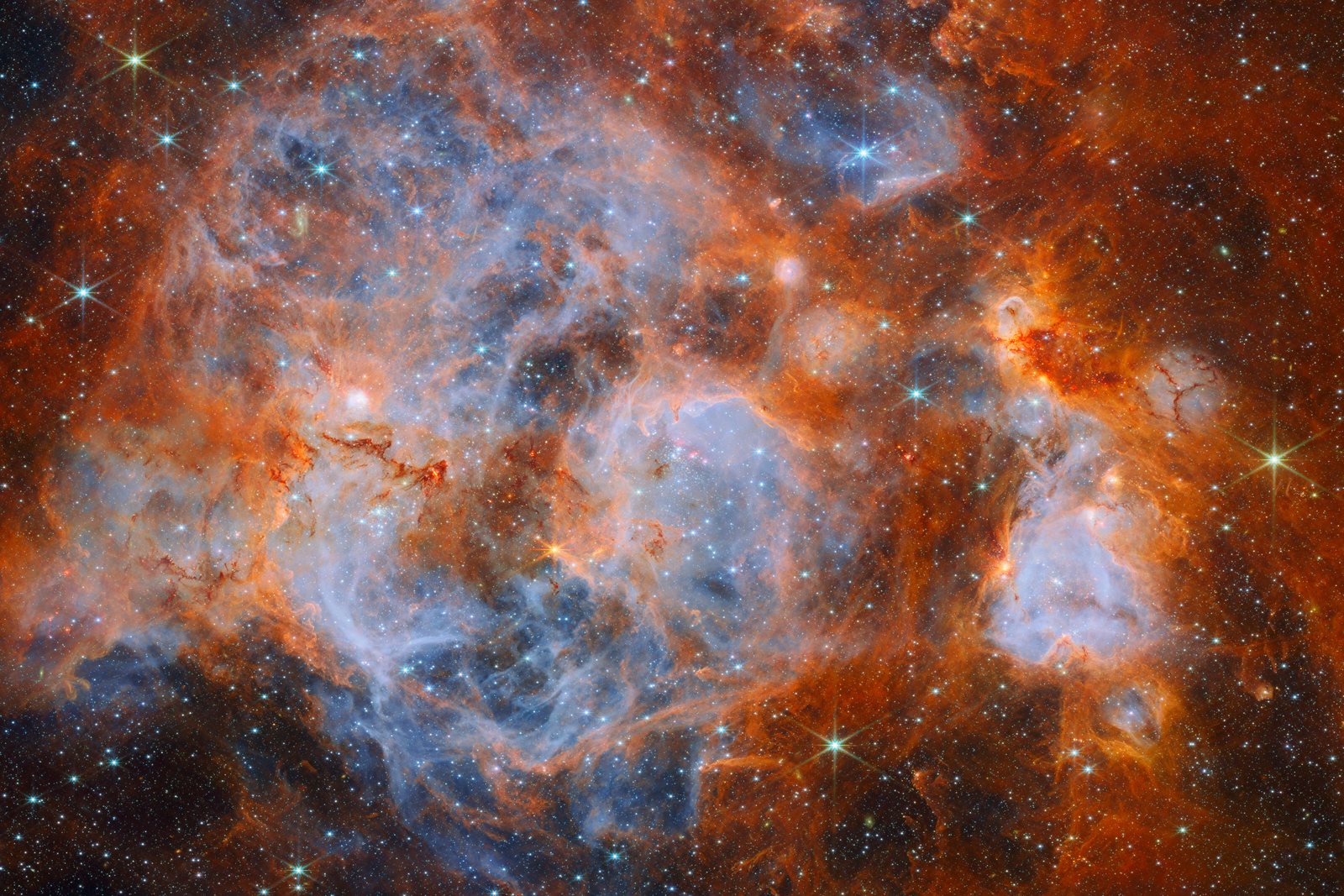 Webb NIRCam image of the N159 star-forming region in the Large Magellanic Cloud: billowing orange clouds surround pale blue bubbles of glowing gas, threaded with dark red filaments and scattered with thousands of stars