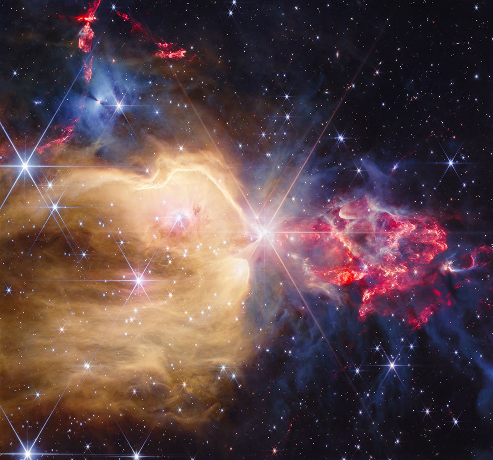 Webb NIRCam image of the NGC 7129 star-forming region — a brilliant yellow star at center with Webb's eight-pointed diffraction spikes, surrounded by a vast golden cavity of glowing gas, a red flame-like plume of dust and protostars, and scattered blue stars